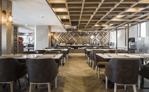 A modern restaurant with a geometric patterned wall, wooden ceiling, and a central counter with a coffee machine. - Zayn Express & Suites (Bangkok)