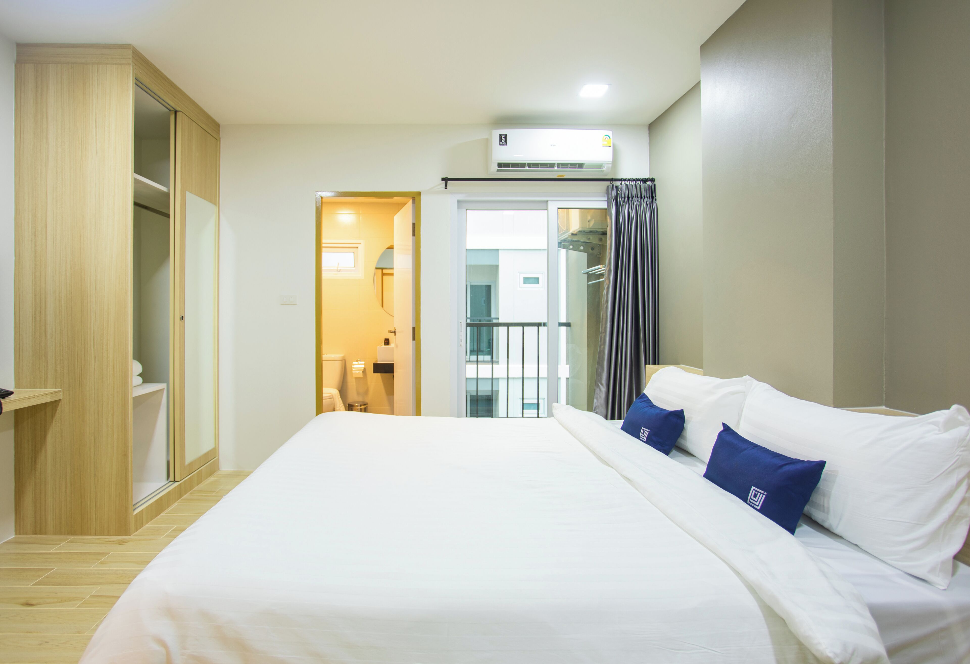 Ein Hotelzimmer mit Bett, Kleiderschrank, Klimaanlage und einem durch eine Glastür sichtbaren Badezimmer.