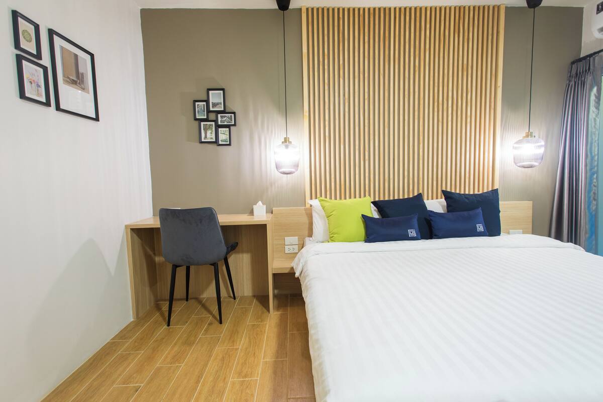 A hotel room with a bed, a desk, a chair, and a wall with framed pictures.