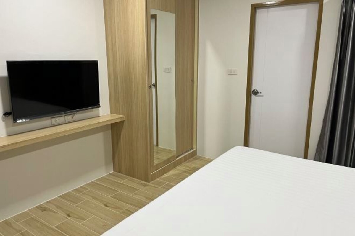 A bedroom with a bed, a TV on a wooden shelf, a door, and a mirror.