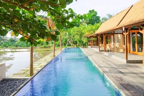 A long swimming pool with a wooden deck on one side and a covered seating area on the other. - Nayaka Living Ubud (Ubud)
