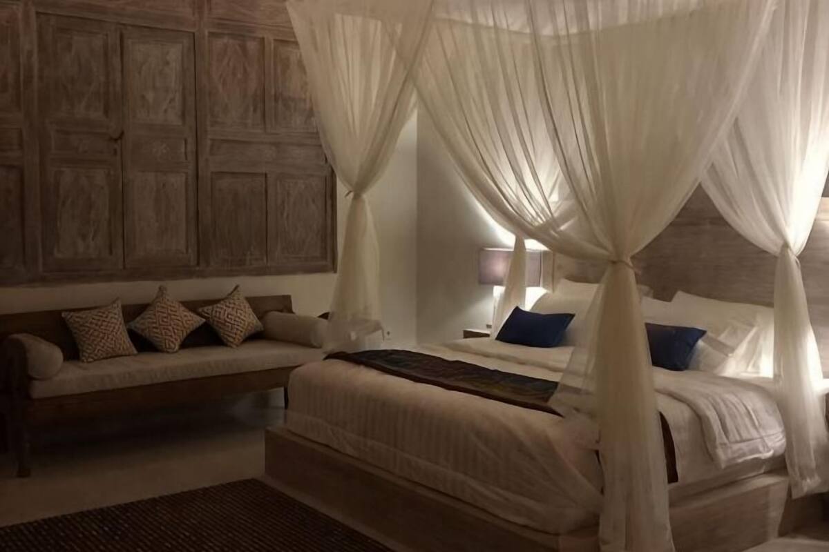 A bedroom with a canopy bed, a sofa, and a nightstand.