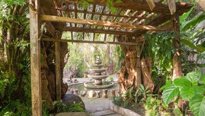 A wooden pergola structure with a stone fountain in the center, surrounded by lush greenery. - Nayaka Living Ubud (Ubud)