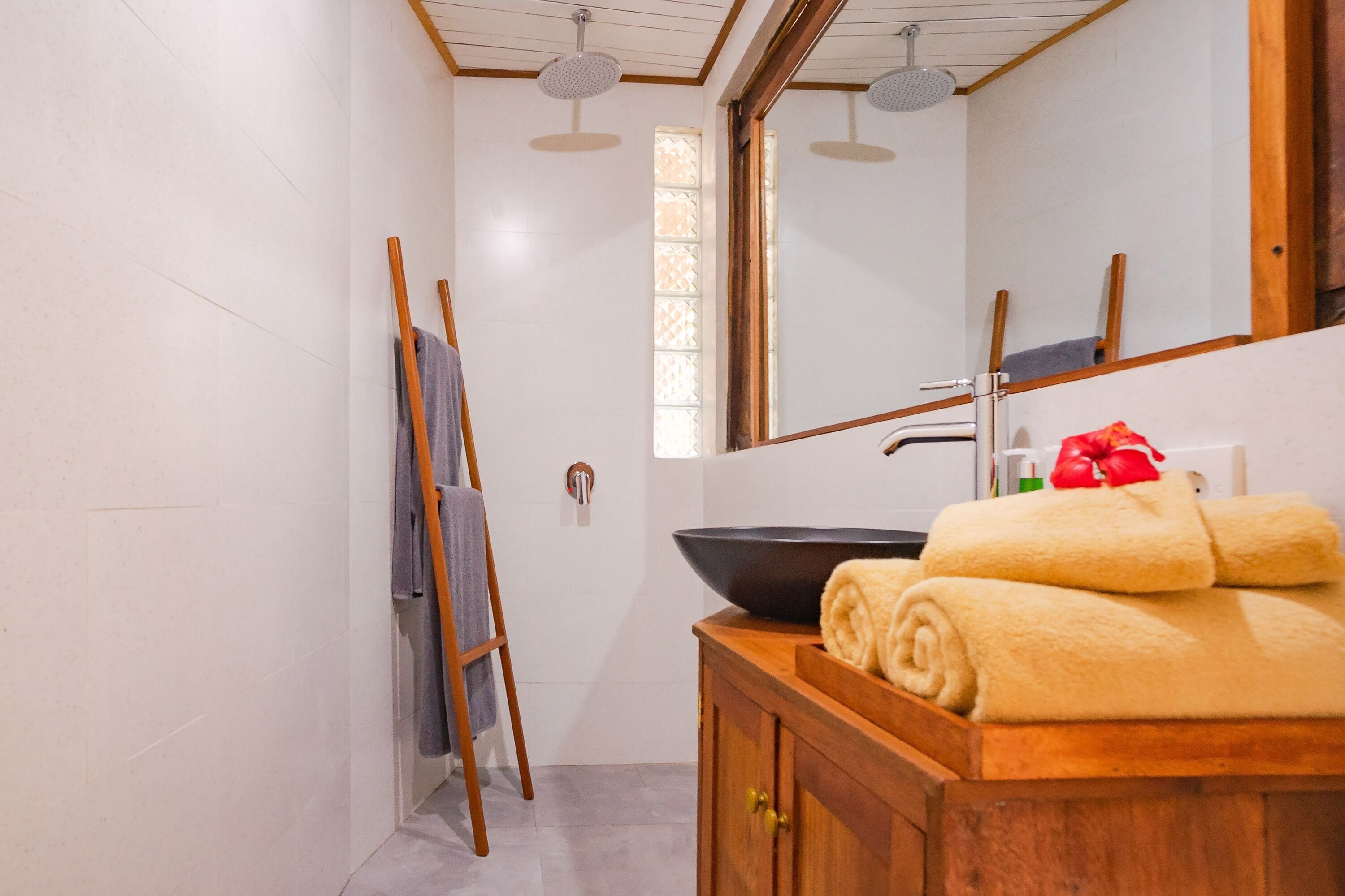 A bathroom with a wooden vanity, a large mirror, a black basin, and towels.