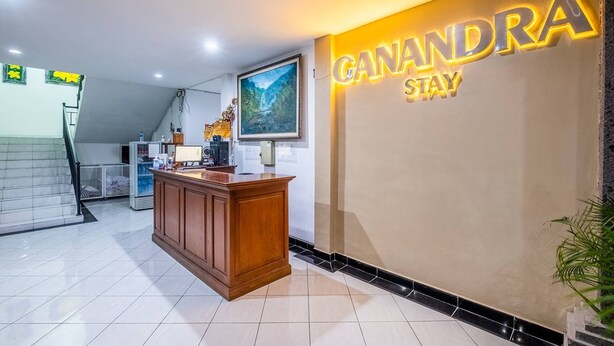 A reception area with a wooden desk, a large framed picture, and a wall sign that reads "CANANDRA STAY". - Ganandra Stay Denpasar (Denpasar)