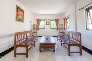 A room with two wooden benches, a central table, and windows with curtains.