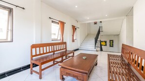 A spacious living area with a wooden bench, a coffee table, and a staircase leading to an upper floor. - Ganandra Stay Denpasar (Denpasar)