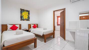 Habitació d'hotel amb dos llits, un capçal de llit de fusta, un bany blanc amb un lavabo i una porta que condueix a una altra habitació.