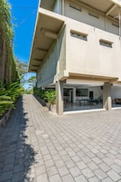 A building with a covered outdoor area, a paved walkway, and greenery along the side.