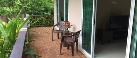 Un patio con una mesa, sillas, un televisor y un cerramiento de vidrio corredizo que da a una habitación.