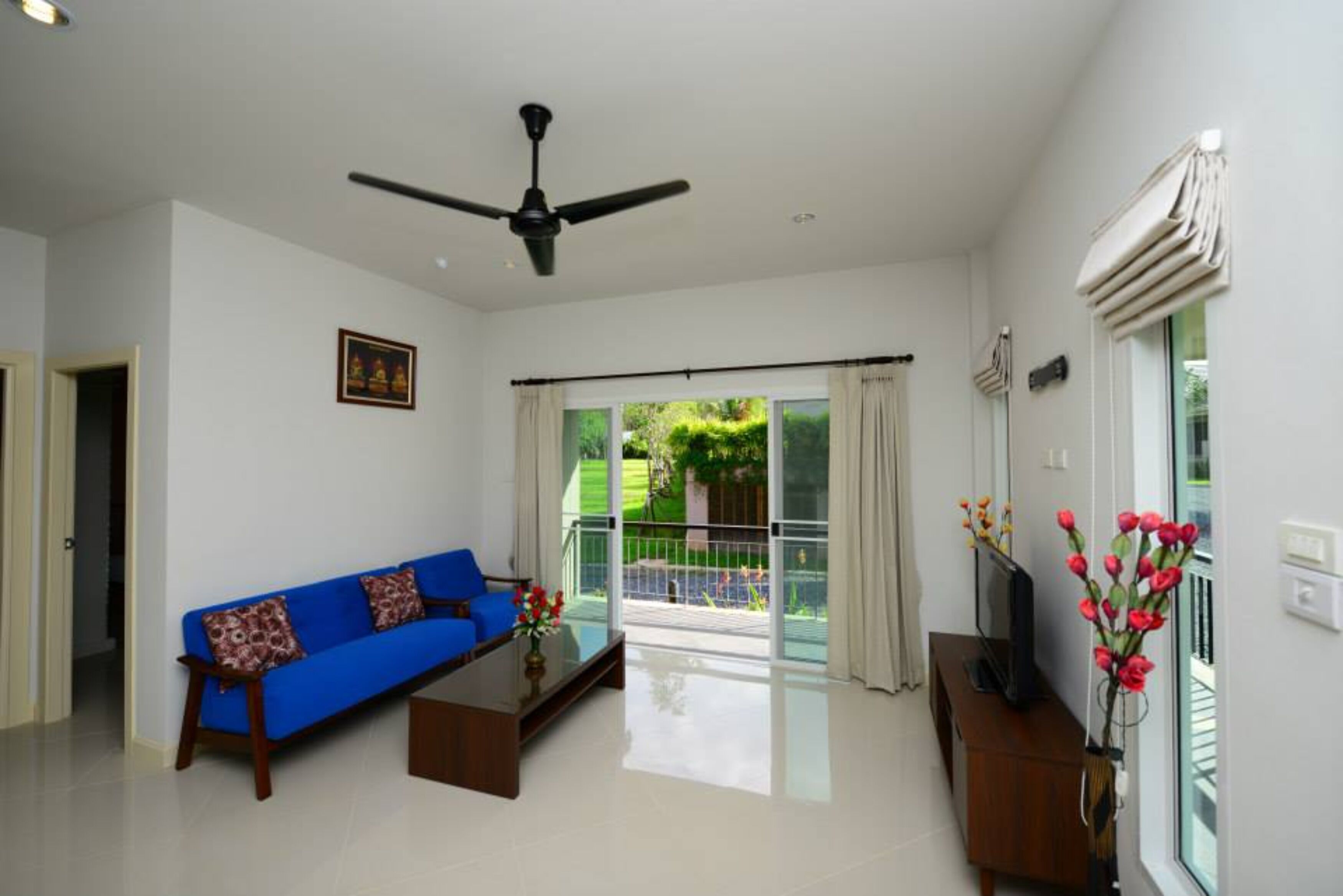 A modern living room with a blue sofa, a coffee table, a television on a wooden stand, and a ceiling fan.