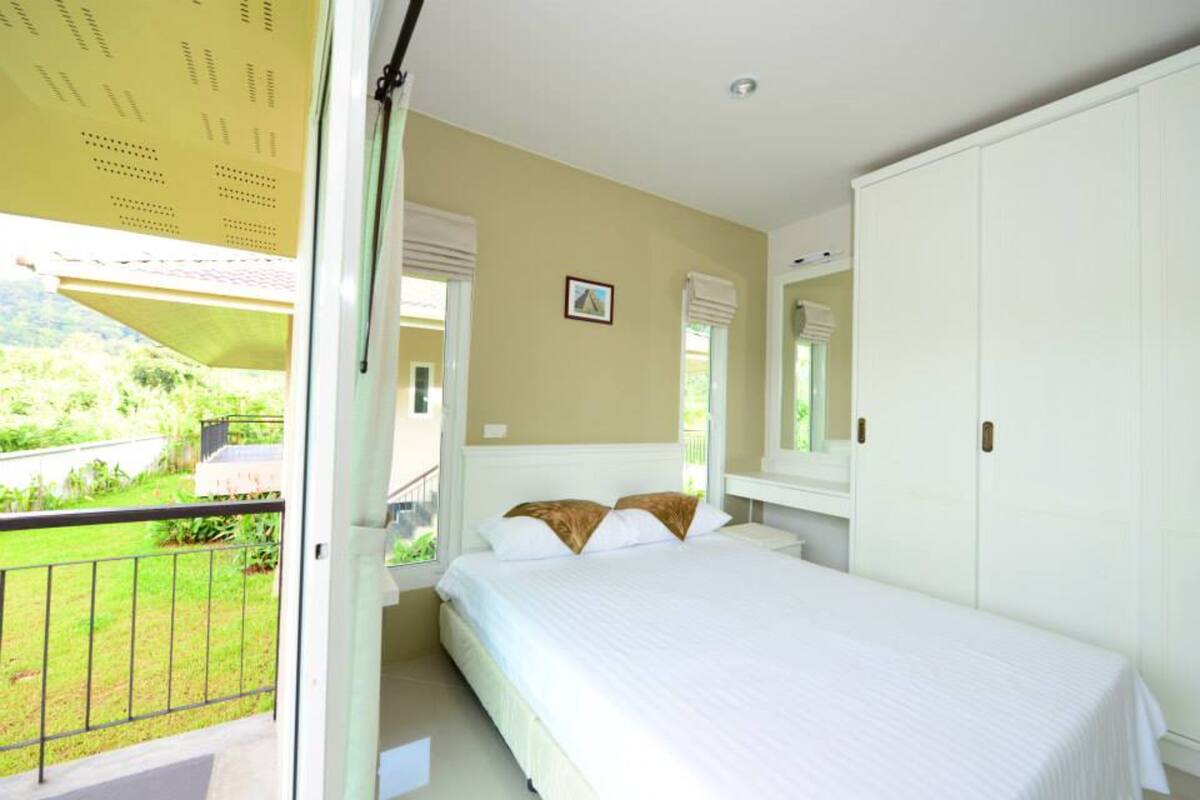 A bedroom with a bed, a window with a view of a green landscape, and a white wardrobe.