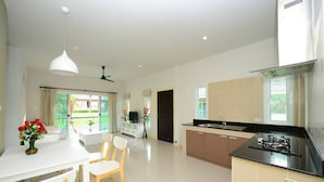 A modern kitchen with a dining area, large windows, and a view of the outdoors. - Bk Villa (Thep Krasattri)