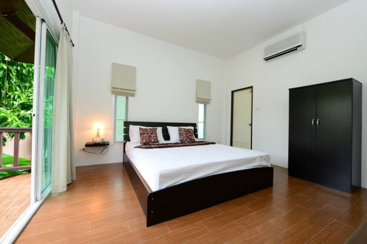 A bedroom with a large bed, a wardrobe, and a window with blinds.