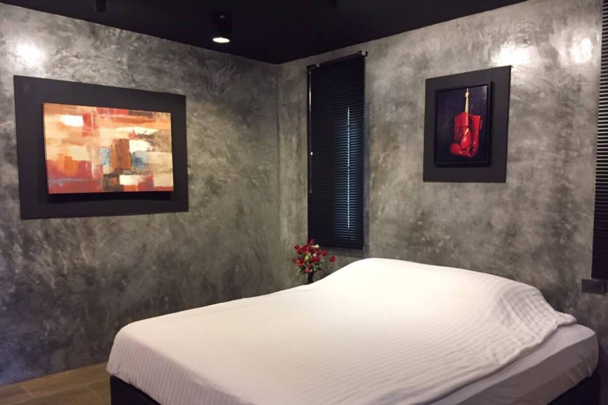 A bedroom with a bed, a window with blinds, and two framed artworks on the walls.