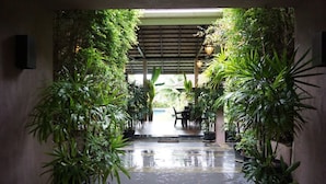 A covered walkway with potted plants on either side, leading to a seating area. - Bk Villa (Thep Krasattri)