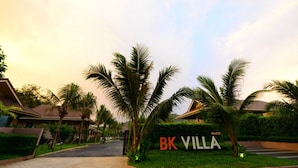 A gated entrance to a property named BK Villa, surrounded by palm trees and a well-maintained lawn. - Bk Villa (Thep Krasattri)
