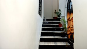 A staircase with black steps and white walls, leading to a landing with a potted plant and a decorative mask. - Paradise Homestay Civil Lines, Only Family & Corporate Stays (Nagpur)