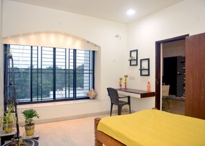 A room with a bed, a desk, a chair, a window with a view, and a door. - Paradise Homestay Civil Lines, Only Family & Corporate Stays (Nagpur)