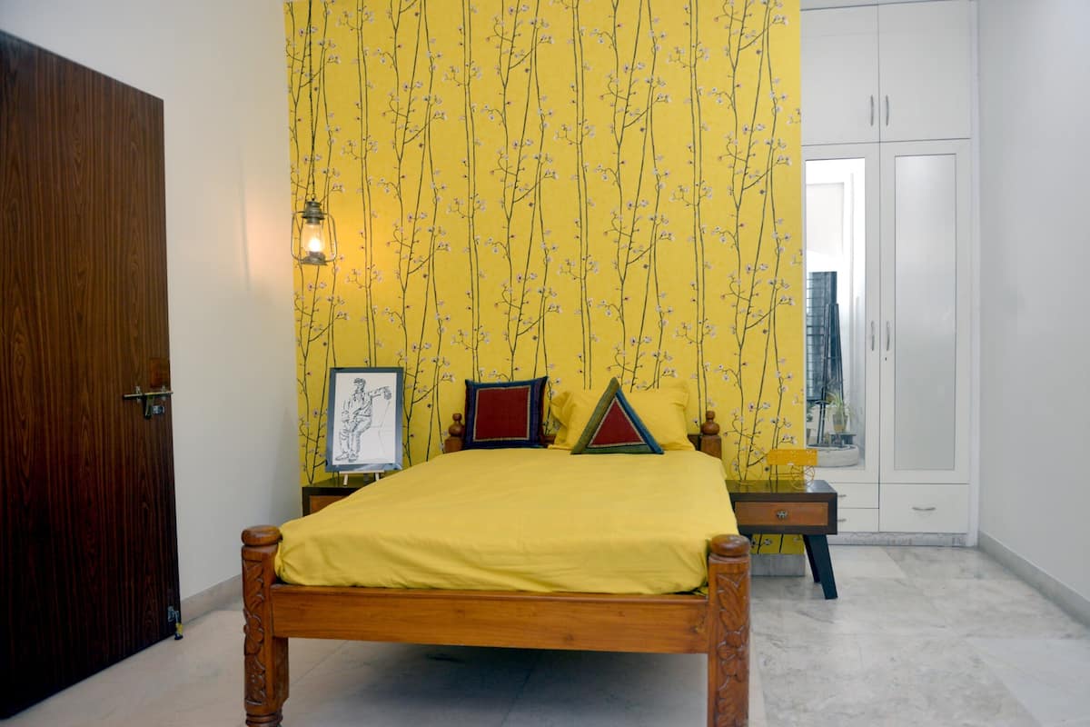 A bedroom with a wooden bed, yellow floral wallpaper, a framed picture on the wall, and a wardrobe.