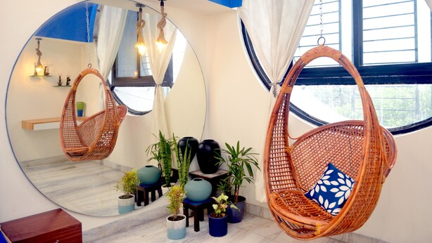 A room with a large mirror, wicker chairs, potted plants, and a view of the outdoors. - Paradise Homestay Civil Lines, Only Family & Corporate Stays (Nagpur)