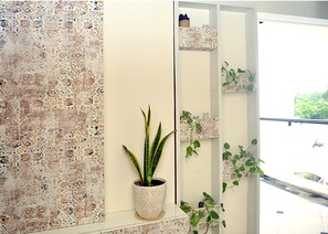 A room with a patterned wall, a potted plant, and a mirror reflecting a balcony with plants and a view of greenery. - Paradise Homestay Civil Lines, Only Family & Corporate Stays (Nagpur)
