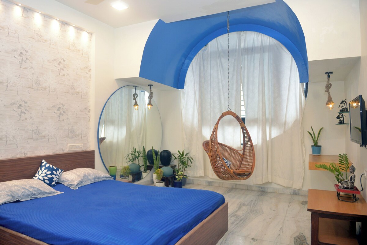 Un dormitorio con cama, una silla colgante y plantas en macetas.