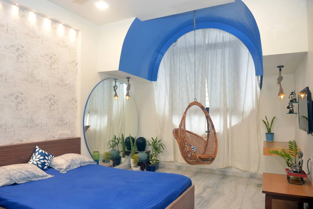 A bedroom with a large bed, a hanging chair, and several potted plants.