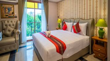 A hotel room with a large bed, a chair, a nightstand, and a view of greenery outside.