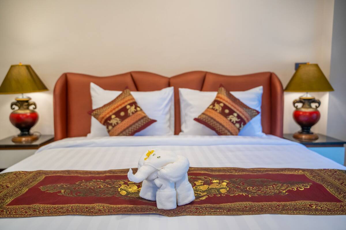 A bed with a red and gold embroidered bedspread, two pillows with intricate patterns, and a white elephant-shaped pillow on a red and gold embroidered runner.