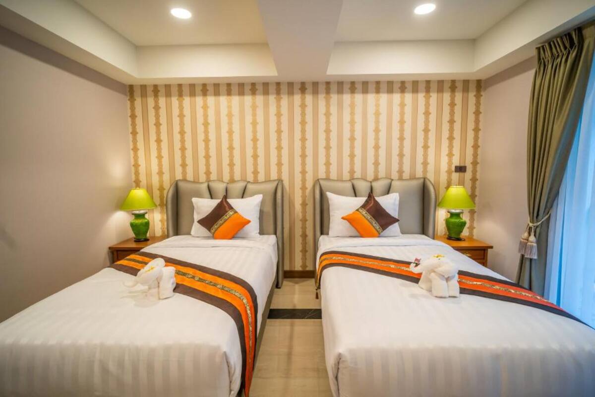 A hotel room with two beds, each with a headboard, pillows, and a small table with a lamp.