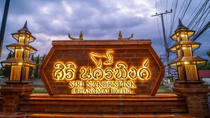 A hotel entrance with a neon sign in a foreign script, two lanterns on either side, and a brick wall.