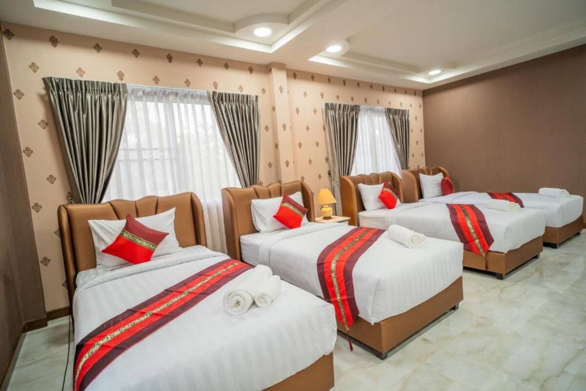 A hotel room with three beds, each with white bedding and red accents.