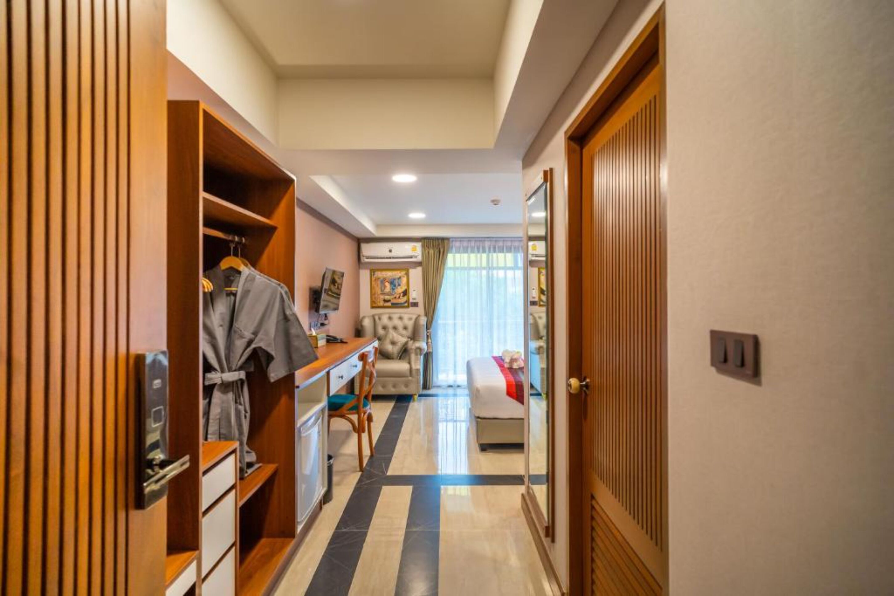 Une chambre d’hôtel avec une armoire en bois, un bureau avec une chaise, un lit recouvert d’une couverture rouge et une fenêtre avec des rideaux.