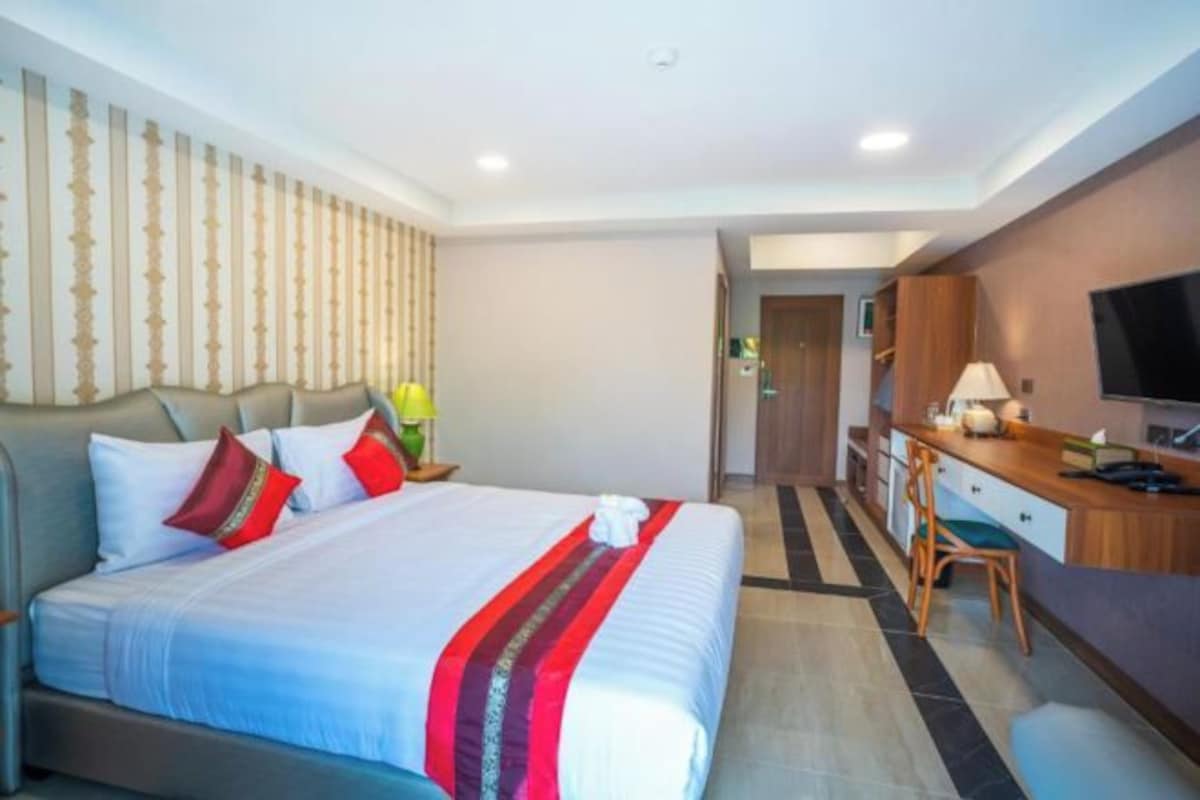A hotel room with a bed, a desk, a chair, a television, and a bathroom visible in the background.