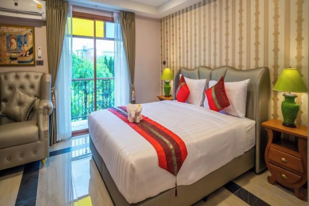 A hotel room with a large bed, a chair, a nightstand, and a view of greenery outside.