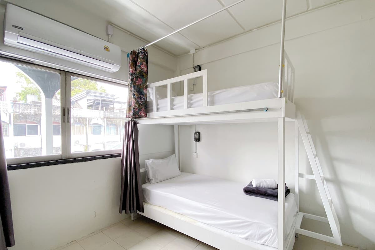 A bunk bed room with a window, air conditioning unit, and a view of buildings outside.