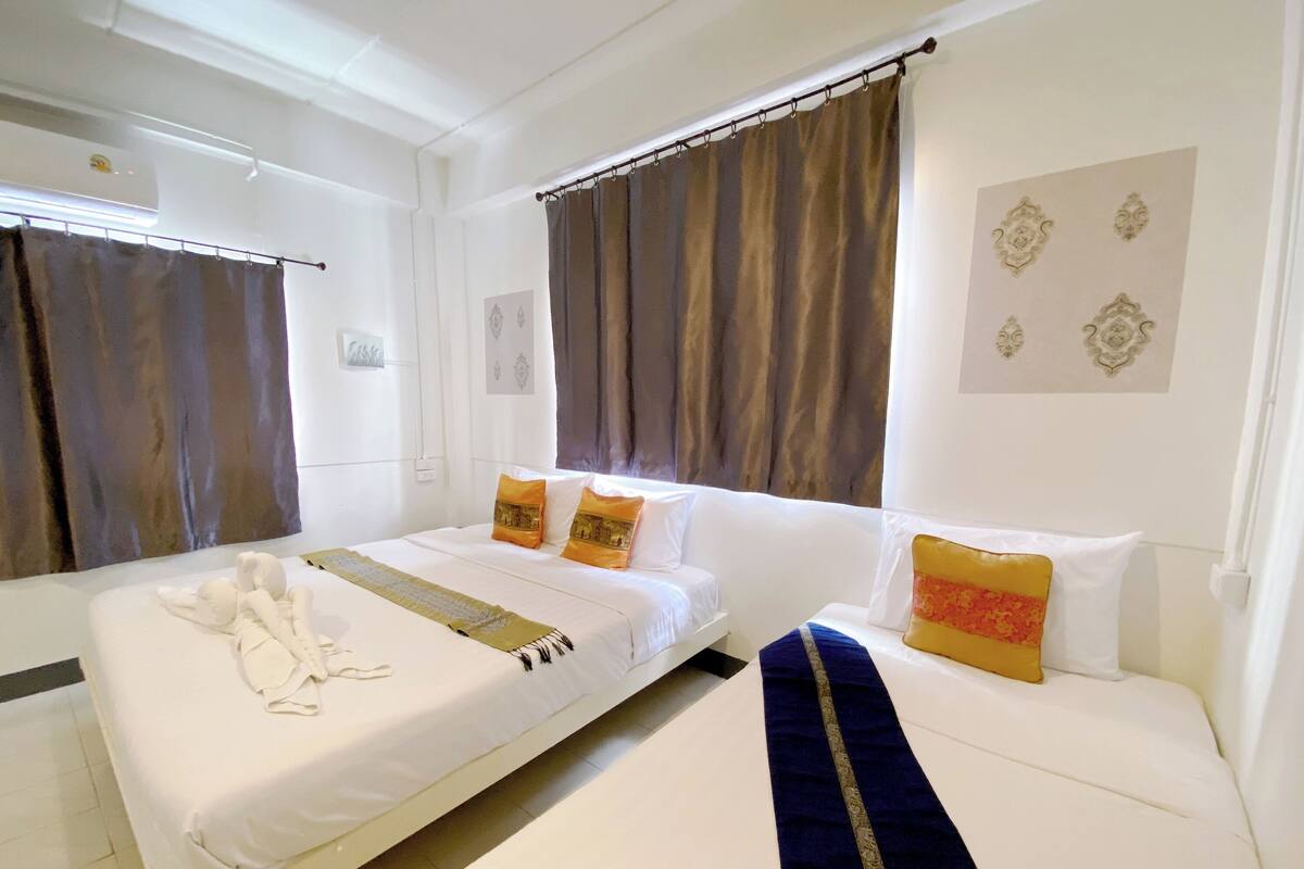 A hotel room with a large bed, a smaller bed, and a sofa. There are curtains on the windows, and a wall decoration above the sofa.