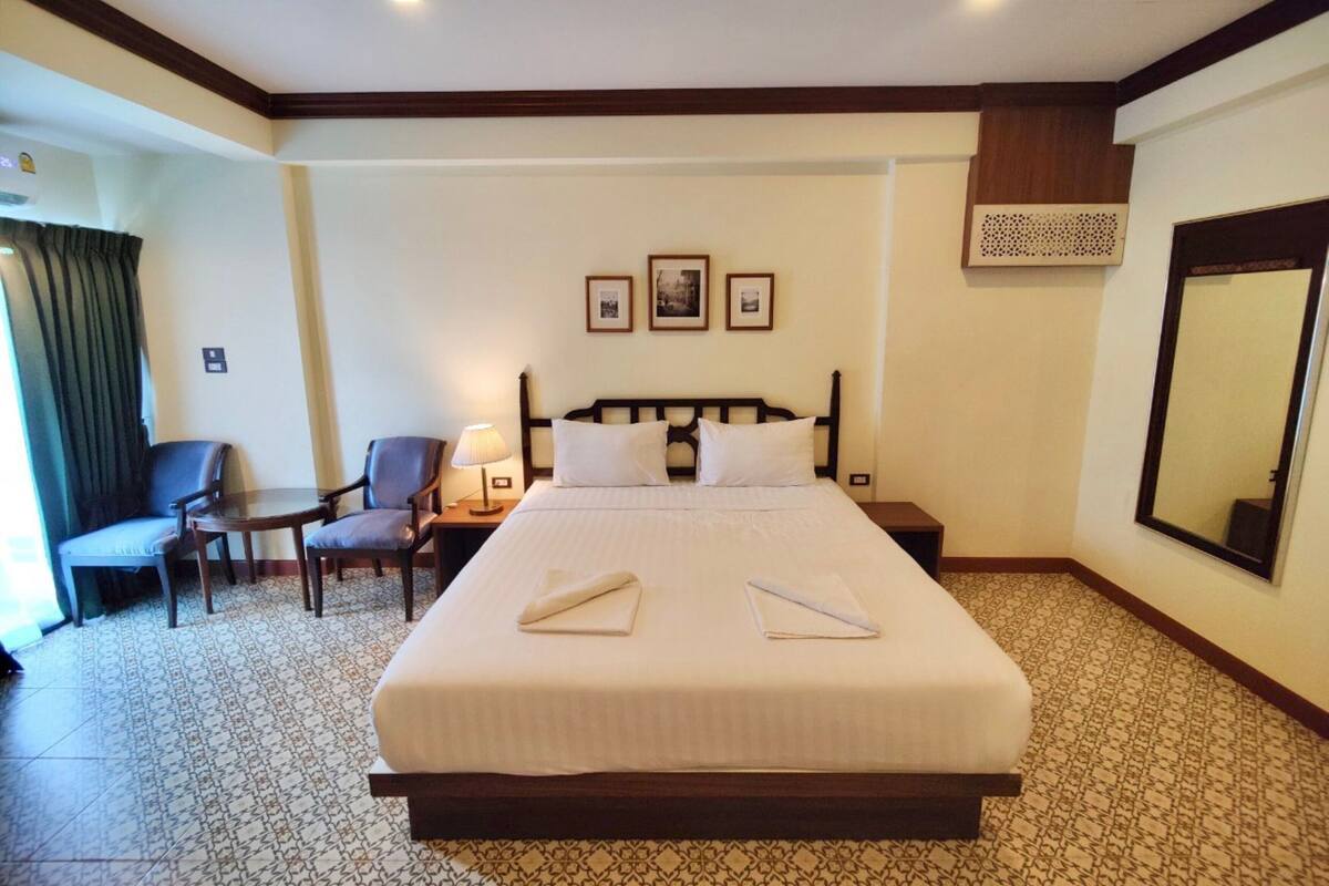 A hotel room with a large bed, two bedside tables, a chair, a desk, and a large mirror.