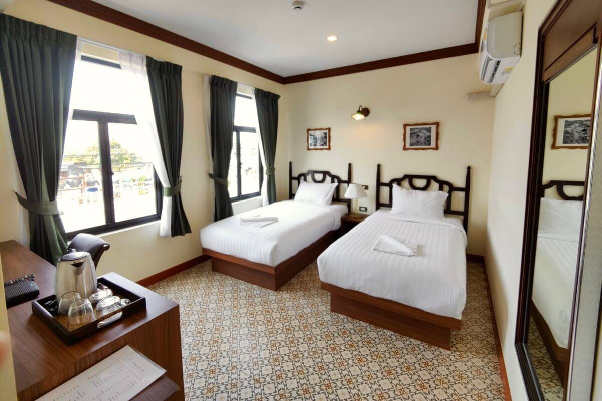 A hotel room with two beds, a desk with a tray of toiletries, and a view of the outside.