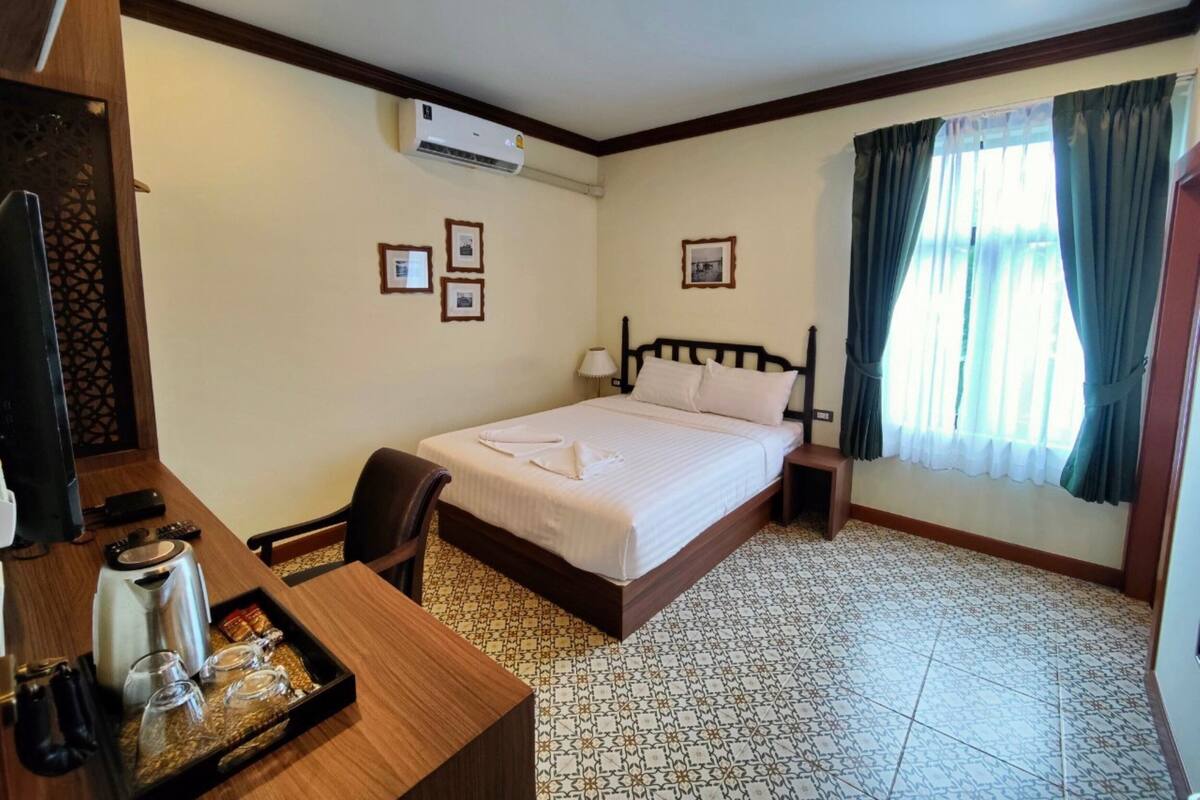 A hotel room with a bed, a desk with a tray of breakfast items, a chair, a TV, and an air conditioner.