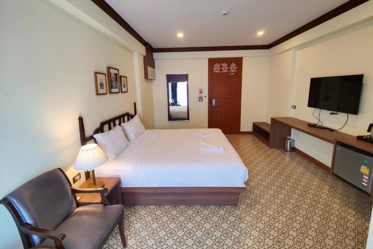 A hotel room with a bed, a desk with a television, a chair, and a patterned carpet.