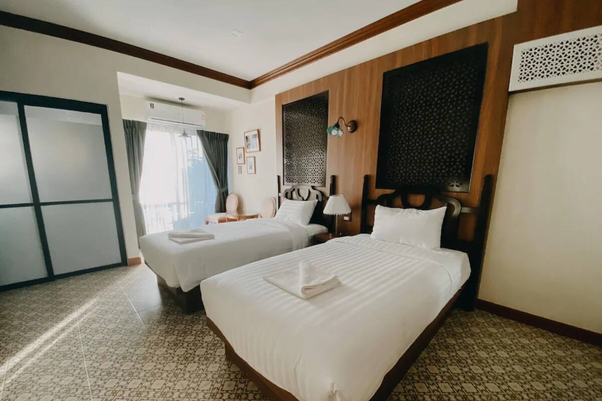 A hotel room with two beds, a large window with curtains, a wall-mounted air conditioner, and a patterned floor.