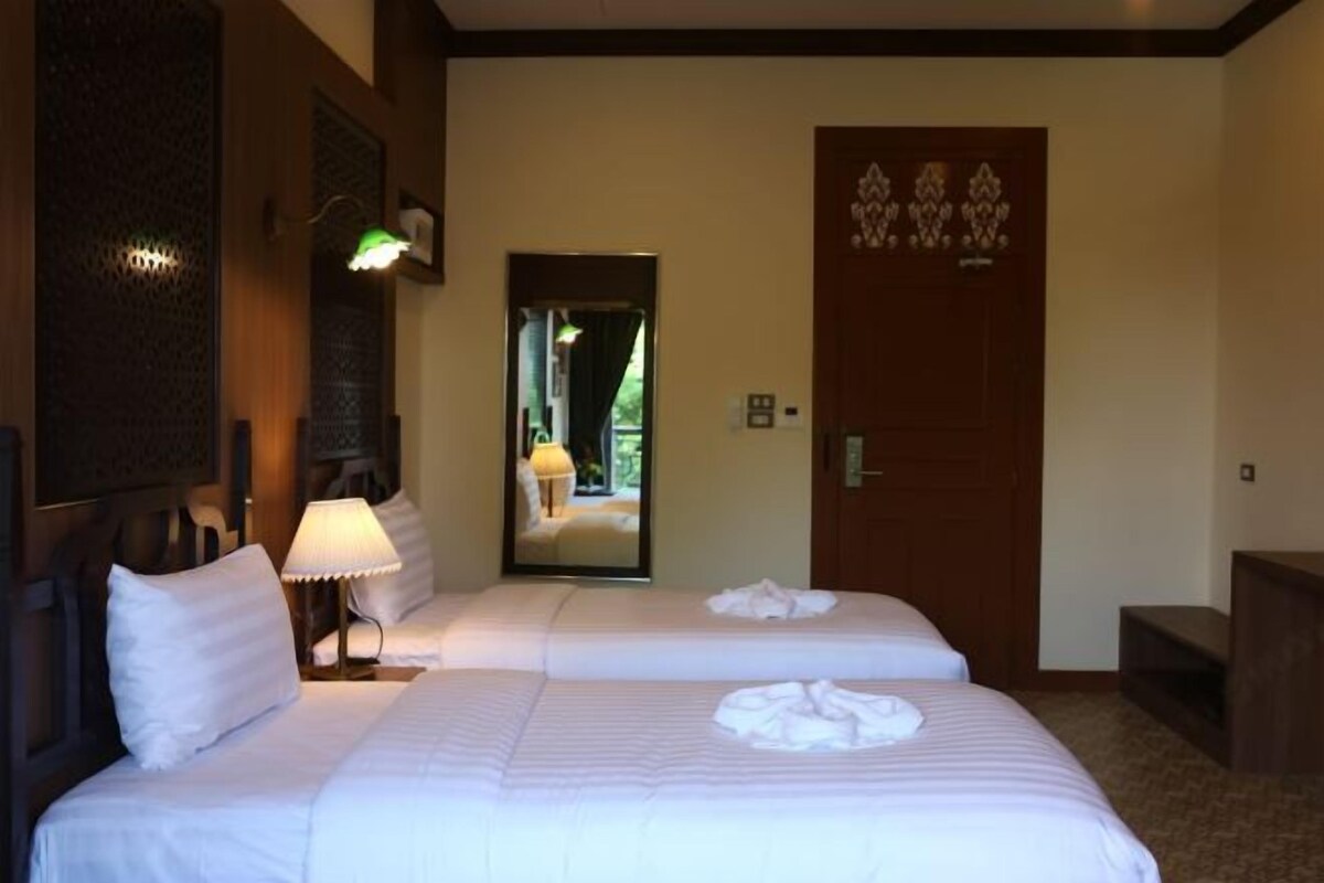 A hotel room with two beds, a mirror, a wooden door, and a lamp.