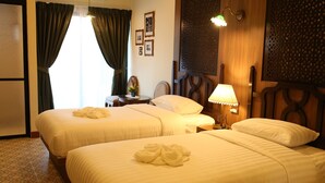 Quarto de hotel com duas camas, uma mesa de cabeceira, uma luminária e um painel decorativo na parede.