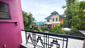 Varanda com grades de metal preto, vista para área residencial com casas e vegetação.