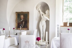 Un comedor con manteles blancos, candelabros y una estatua de una mujer.