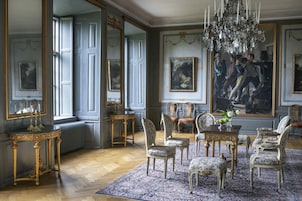 Una sala amplia con muebles elaborados, un candelabro y grandes cuadros enmarcados.