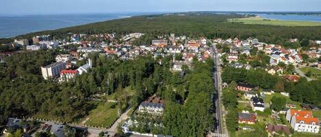 Une vue aérienne d’une ville côtière, avec un mélange de bâtiments résidentiels et un hôtel imposant, doté de plusieurs étages et de balcons.