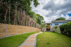 Um jardim bem cuidado com um caminho de pedra que leva a uma casa de fachada azul e chaminé visível.